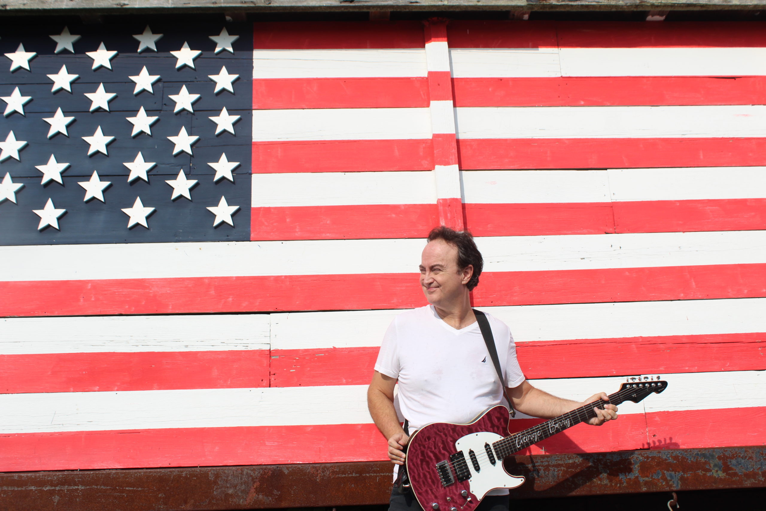 This is a picture of Geroge A. Barry with his elecric guitar in front of the american flag